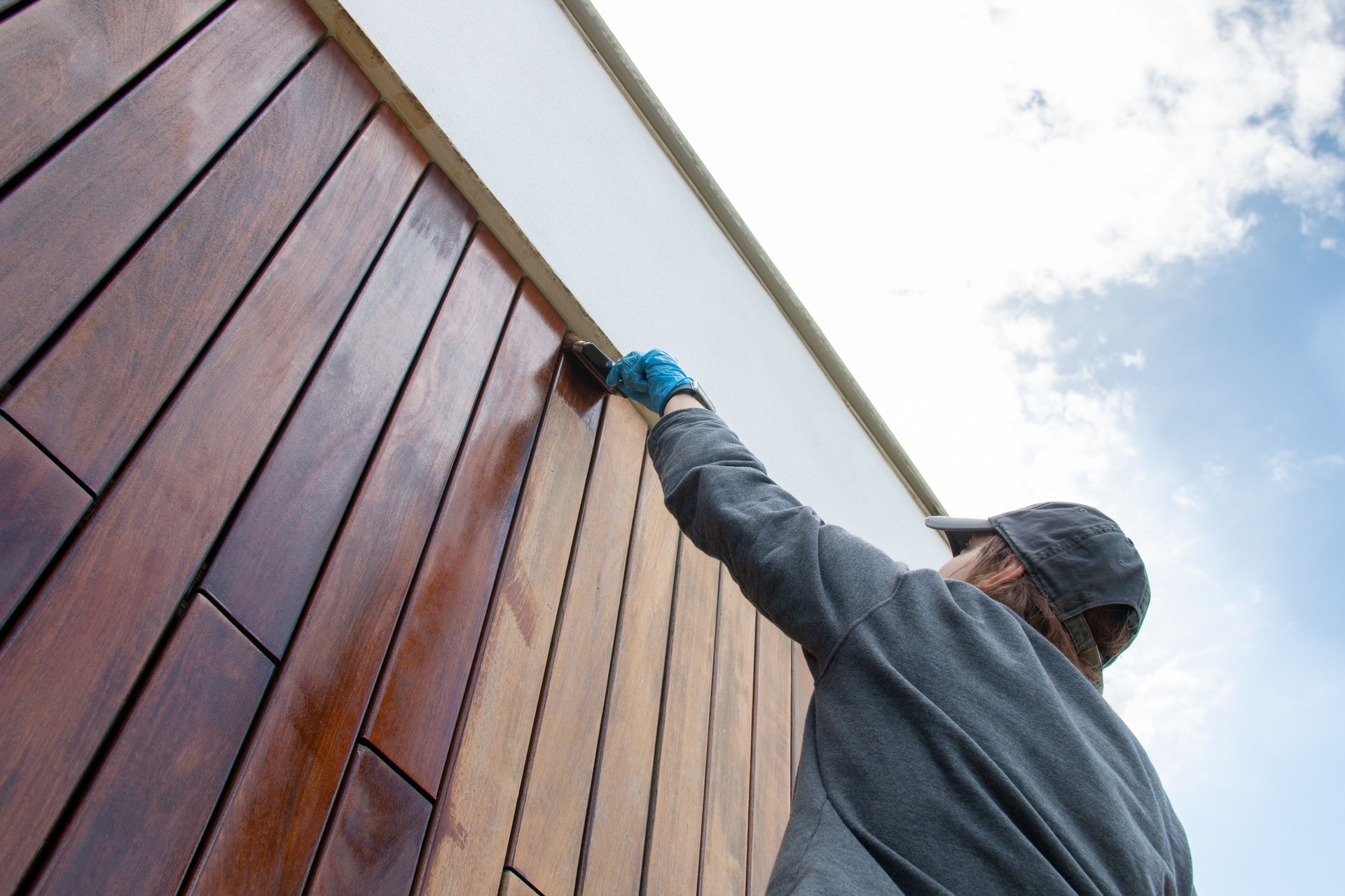 Staining the wood facade cladding with paint brush and protective oil, stain, house improvement copy space, looking up perspective angle